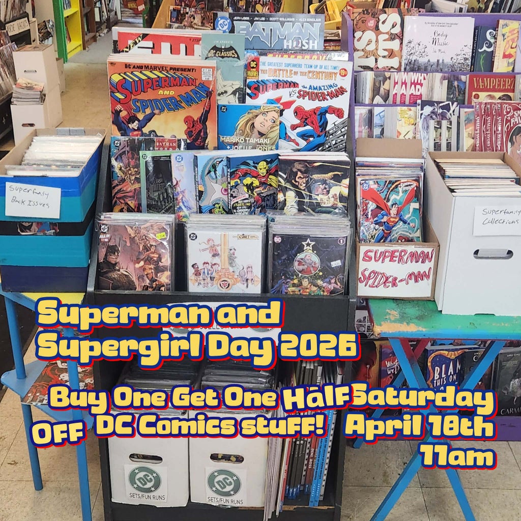 a picture taken on sales floor of comics n'more showing our superman day display of stuff you can buy. in yelllow, red and blue font is a caption reading Superman and Supergirl Day 2026. Buy One Get one Half Off DC Comics Stuff. Saturday, April 18th 11am